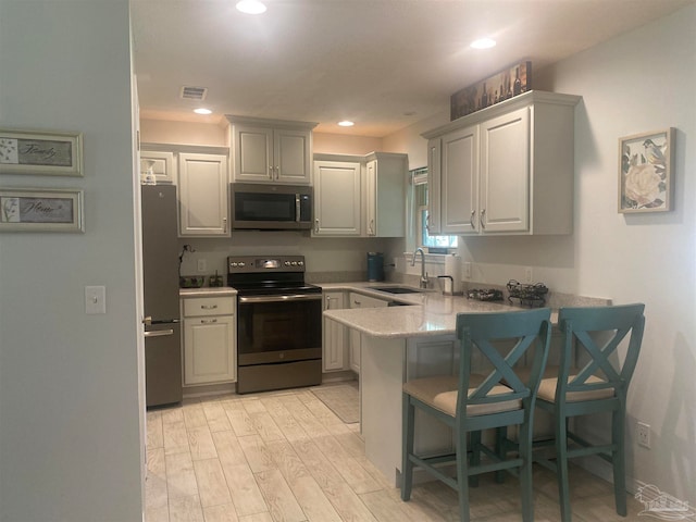 kitchen with appliances with stainless steel finishes, sink, a kitchen bar, kitchen peninsula, and light hardwood / wood-style floors