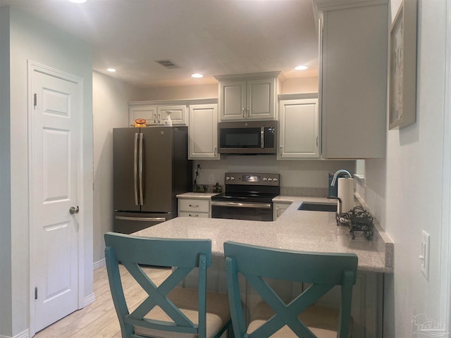 kitchen featuring kitchen peninsula, appliances with stainless steel finishes, a kitchen bar, light hardwood / wood-style floors, and sink