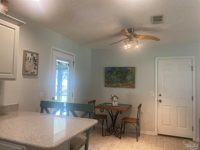 dining space with a textured ceiling, light wood-type flooring, and ceiling fan