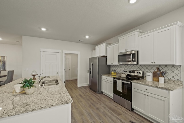 kitchen with sink, white cabinetry, light stone countertops, decorative backsplash, and stainless steel appliances