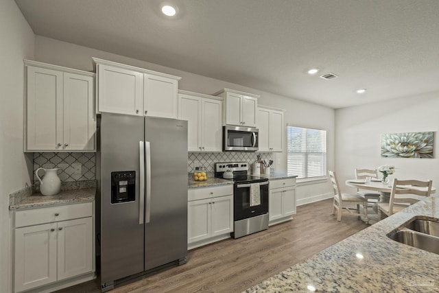 kitchen with light stone counters, hardwood / wood-style flooring, white cabinets, and stainless steel appliances