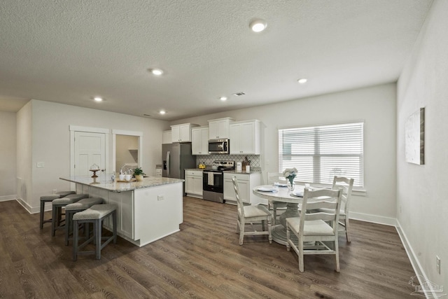 kitchen with light stone countertops, appliances with stainless steel finishes, a kitchen island with sink, white cabinets, and a breakfast bar area