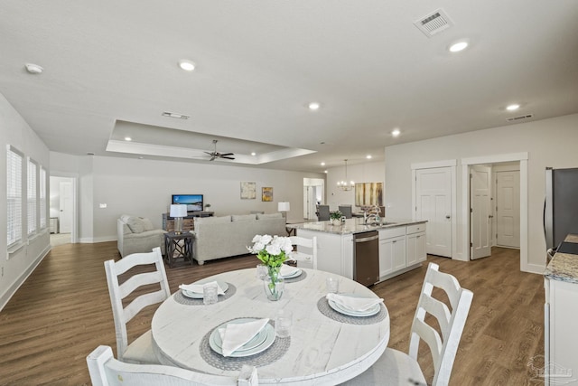 dining space with sink, dark hardwood / wood-style flooring, ceiling fan with notable chandelier, and a raised ceiling