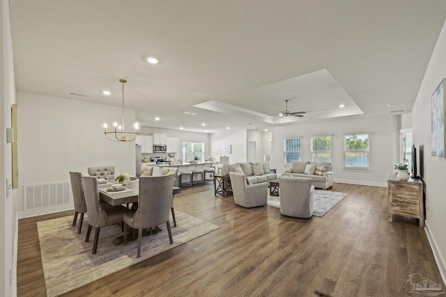 dining area featuring ceiling fan with notable chandelier, a raised ceiling, and dark hardwood / wood-style flooring