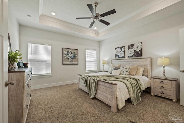 carpeted bedroom with ceiling fan, a raised ceiling, and multiple windows