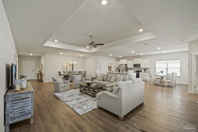 living room with a textured ceiling, ceiling fan with notable chandelier, a tray ceiling, and dark hardwood / wood-style flooring