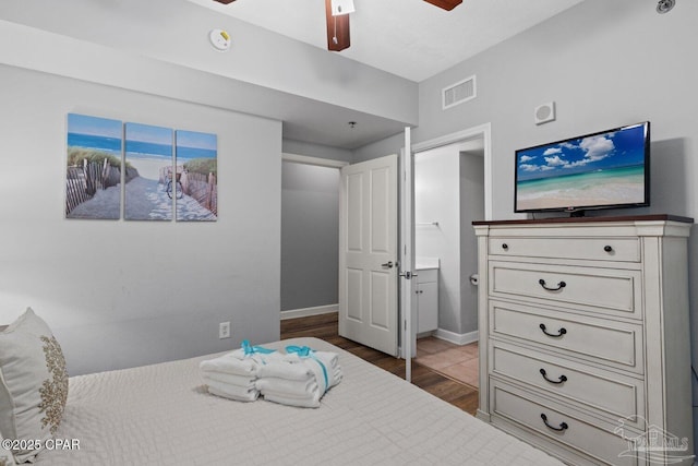 bedroom with wood finished floors, visible vents, ensuite bath, baseboards, and ceiling fan