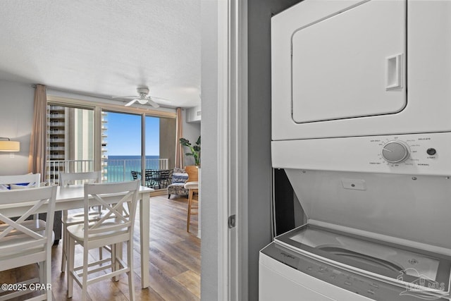 laundry room with a ceiling fan, wood finished floors, a textured ceiling, stacked washing maching and dryer, and a water view