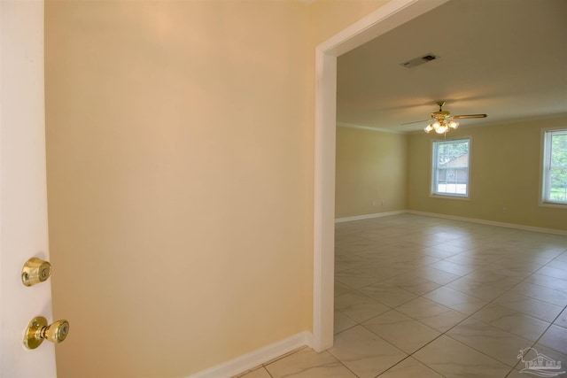 spare room featuring light tile patterned floors, a ceiling fan, visible vents, baseboards, and ornamental molding