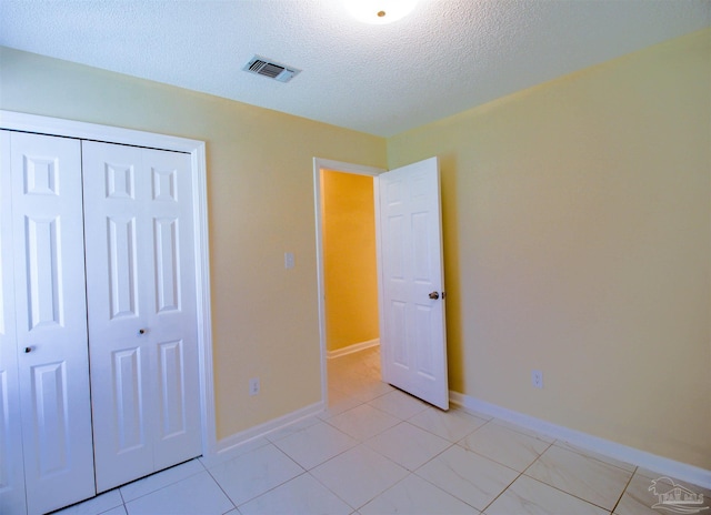 unfurnished bedroom with a textured ceiling, a closet, visible vents, and baseboards