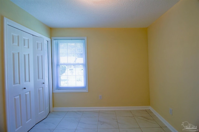 unfurnished bedroom featuring a textured ceiling, baseboards, and a closet