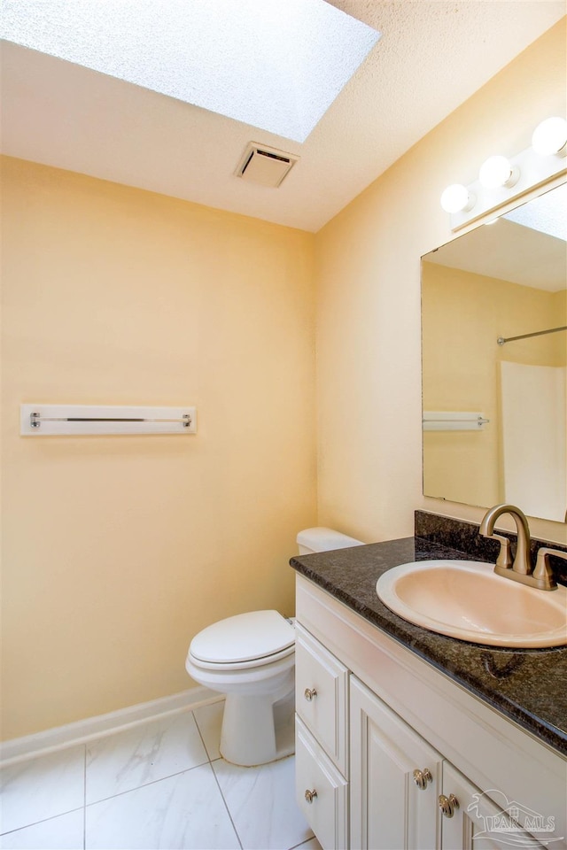 full bathroom with toilet, a skylight, vanity, visible vents, and baseboards