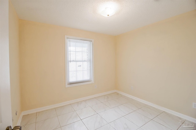 spare room with light tile patterned floors, baseboards, and a textured ceiling