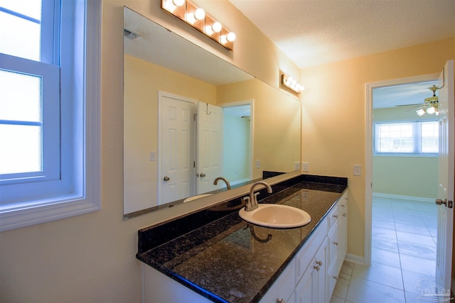 bathroom with a textured ceiling, ceiling fan, tile patterned flooring, vanity, and baseboards