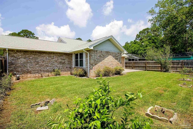 view of side of property featuring a yard, brick siding, a shingled roof, and fence