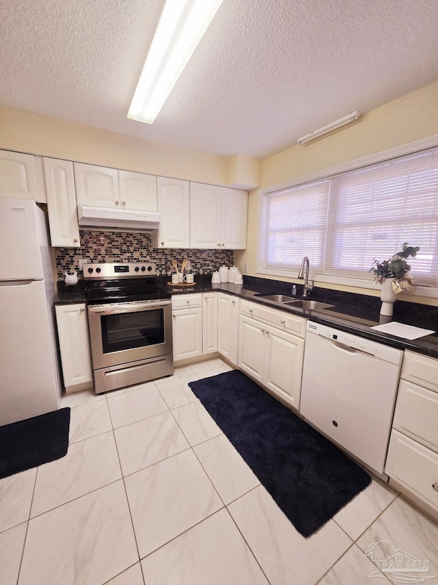 kitchen featuring white appliances, dark countertops, a sink, and under cabinet range hood