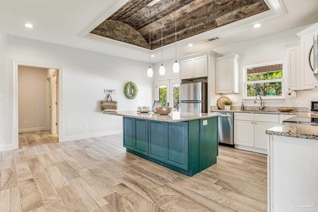 kitchen featuring a kitchen island, appliances with stainless steel finishes, a tray ceiling, and white cabinetry