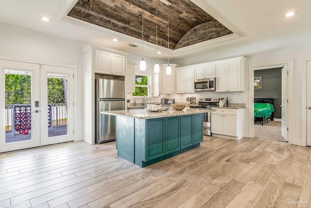 kitchen with appliances with stainless steel finishes, french doors, a raised ceiling, white cabinets, and a kitchen island