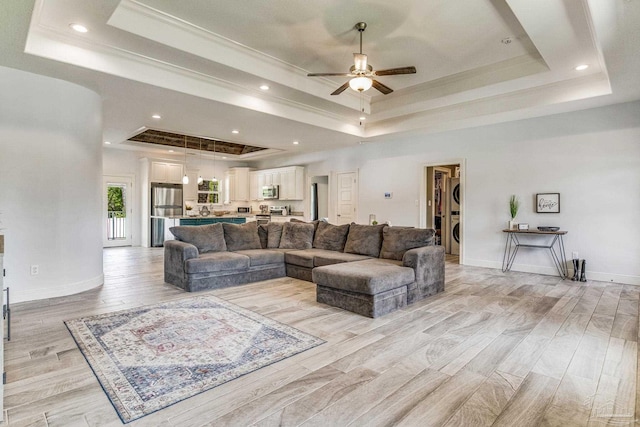 living room with light hardwood / wood-style flooring, ceiling fan, a raised ceiling, and stacked washer and dryer