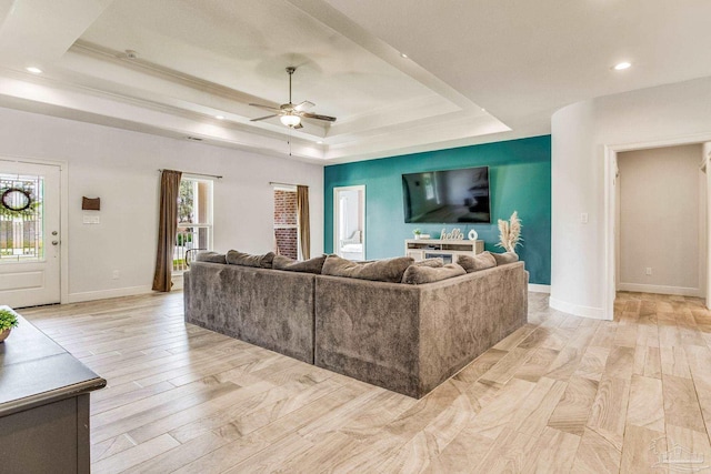 living room featuring light wood-type flooring, a raised ceiling, and ceiling fan