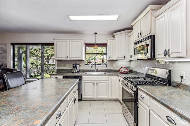 kitchen featuring sink, decorative light fixtures, light tile patterned floors, appliances with stainless steel finishes, and white cabinets