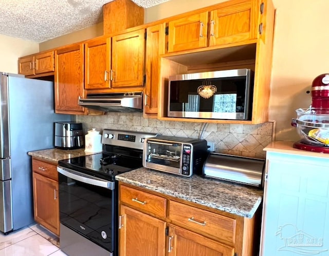 kitchen with a textured ceiling, light tile patterned floors, tasteful backsplash, appliances with stainless steel finishes, and dark stone countertops