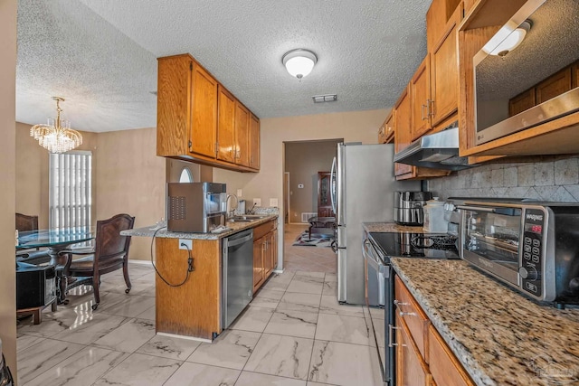 kitchen featuring light stone countertops, a chandelier, hanging light fixtures, stainless steel appliances, and sink