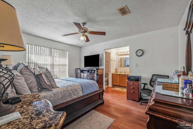 bedroom with ensuite bath, a textured ceiling, ceiling fan, and light hardwood / wood-style flooring