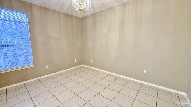 empty room with an inviting chandelier, light tile patterned floors, and baseboards