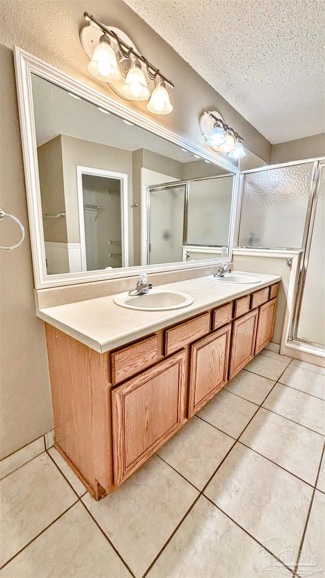 bathroom featuring double vanity, a stall shower, tile patterned floors, a textured ceiling, and a sink