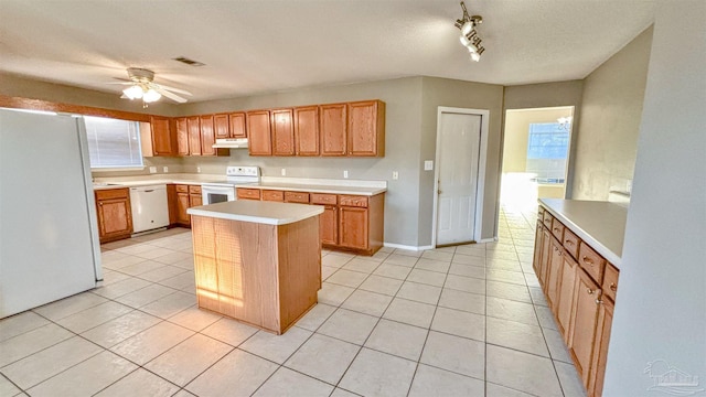 kitchen featuring white appliances, a kitchen island, brown cabinets, light countertops, and under cabinet range hood