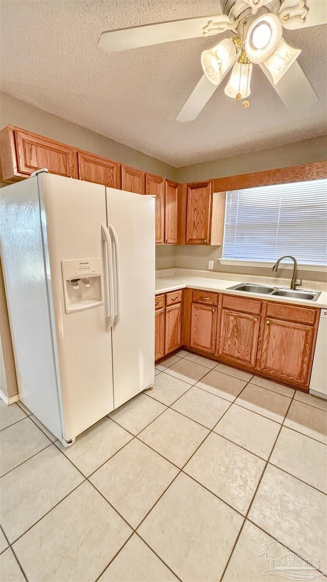 kitchen with light tile patterned flooring, white appliances, a sink, light countertops, and brown cabinets