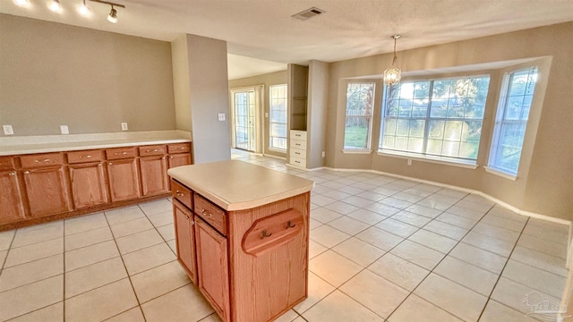 kitchen with decorative light fixtures, light tile patterned floors, light countertops, visible vents, and a kitchen island