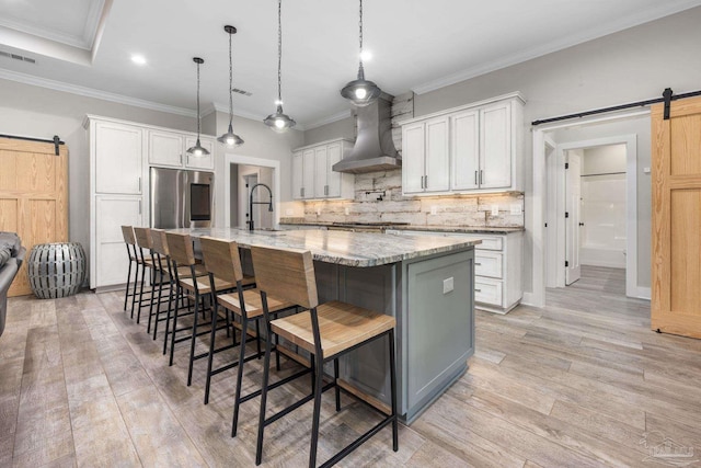 kitchen with a barn door, wall chimney range hood, and white cabinetry