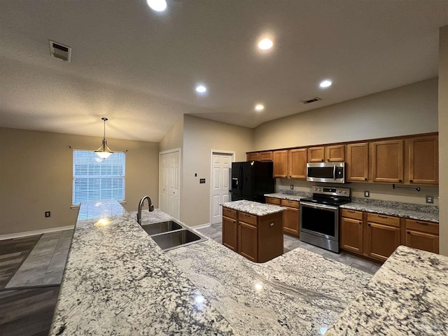 kitchen with light stone counters, pendant lighting, stainless steel appliances, a center island with sink, and sink