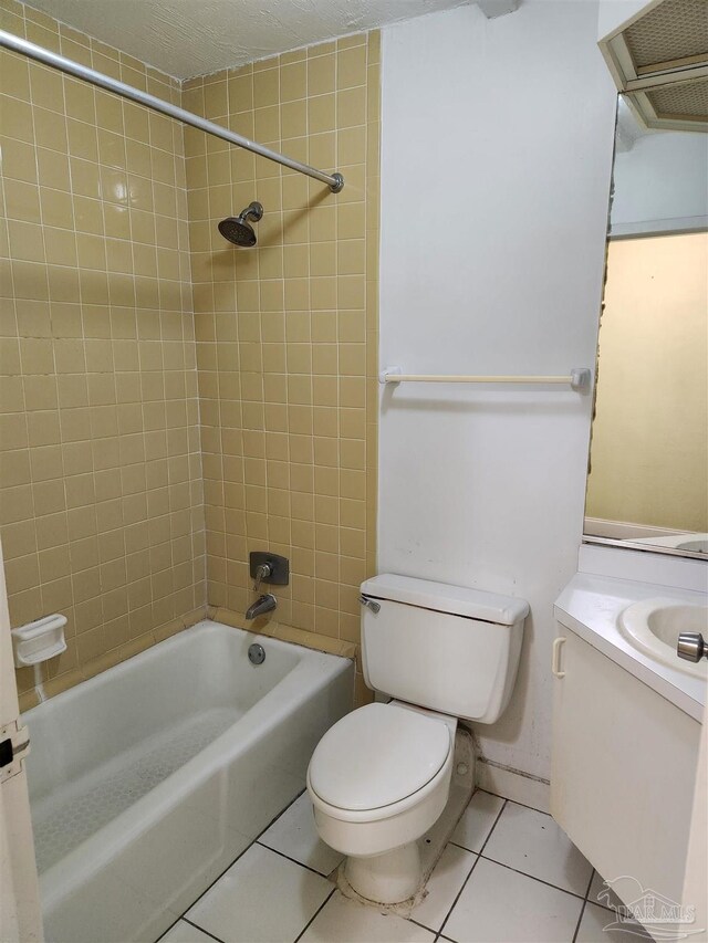 full bathroom with tiled shower / bath combo, tile patterned floors, a textured ceiling, toilet, and vanity