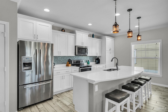 kitchen with a center island with sink, white cabinets, sink, appliances with stainless steel finishes, and decorative light fixtures