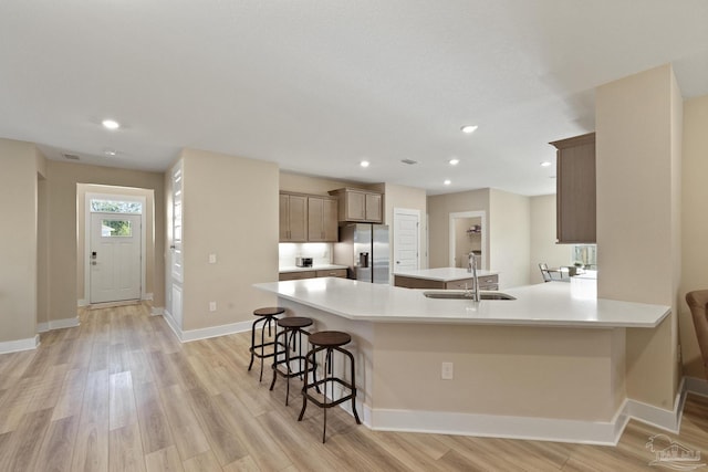 kitchen with sink, a kitchen breakfast bar, kitchen peninsula, stainless steel fridge, and light wood-type flooring