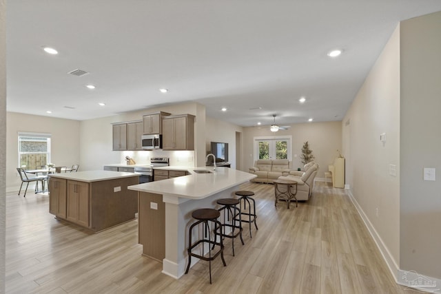 kitchen featuring sink, stainless steel appliances, light hardwood / wood-style flooring, kitchen peninsula, and a kitchen bar