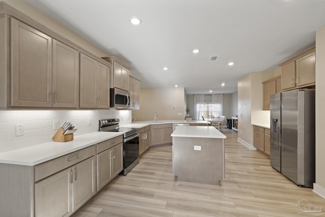 kitchen featuring kitchen peninsula, stainless steel appliances, sink, light hardwood / wood-style floors, and a kitchen island