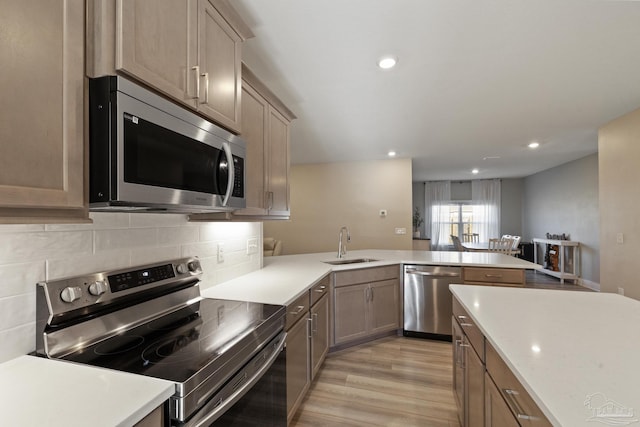 kitchen with kitchen peninsula, sink, light wood-type flooring, and stainless steel appliances