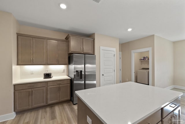 kitchen with stainless steel fridge with ice dispenser, washer / clothes dryer, decorative backsplash, a kitchen island, and light wood-type flooring