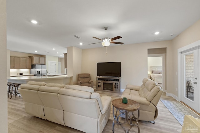 living room featuring ceiling fan, light wood-type flooring, and a fireplace