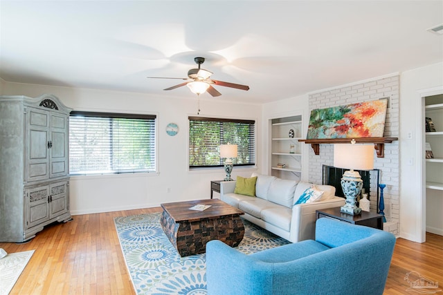 living room featuring a brick fireplace, light hardwood / wood-style flooring, ceiling fan, and built in shelves