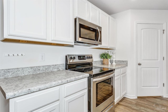 kitchen featuring white cabinetry, light wood-type flooring, stainless steel appliances, and light stone countertops