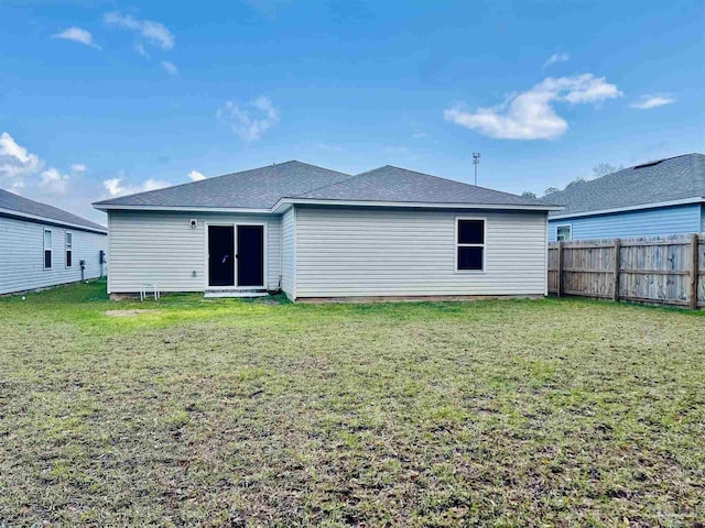 rear view of property featuring a yard, fence, and a shingled roof