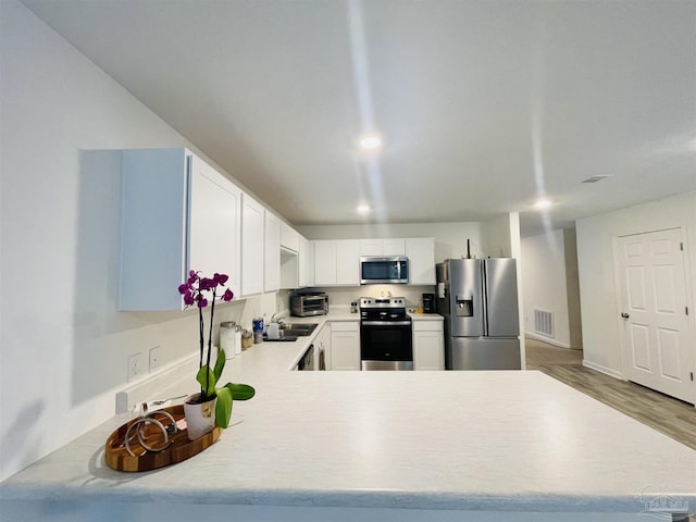 kitchen featuring visible vents, a peninsula, a sink, stainless steel appliances, and light countertops