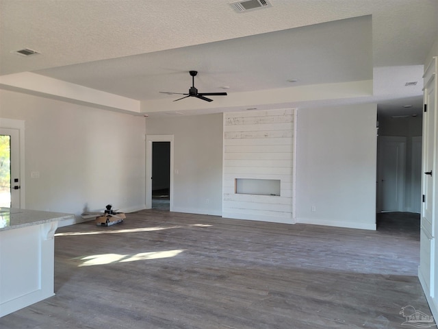 unfurnished living room featuring a large fireplace, hardwood / wood-style flooring, a raised ceiling, and ceiling fan