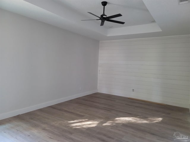 empty room with a raised ceiling, ceiling fan, and hardwood / wood-style floors