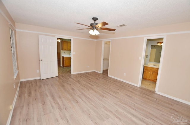 unfurnished bedroom with a textured ceiling, connected bathroom, visible vents, light wood-type flooring, and a walk in closet